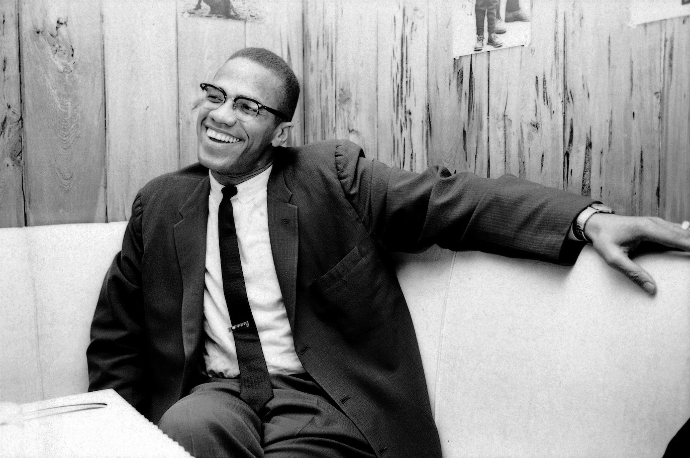 Black and white photo of Malcolm X laughing in a booth table.