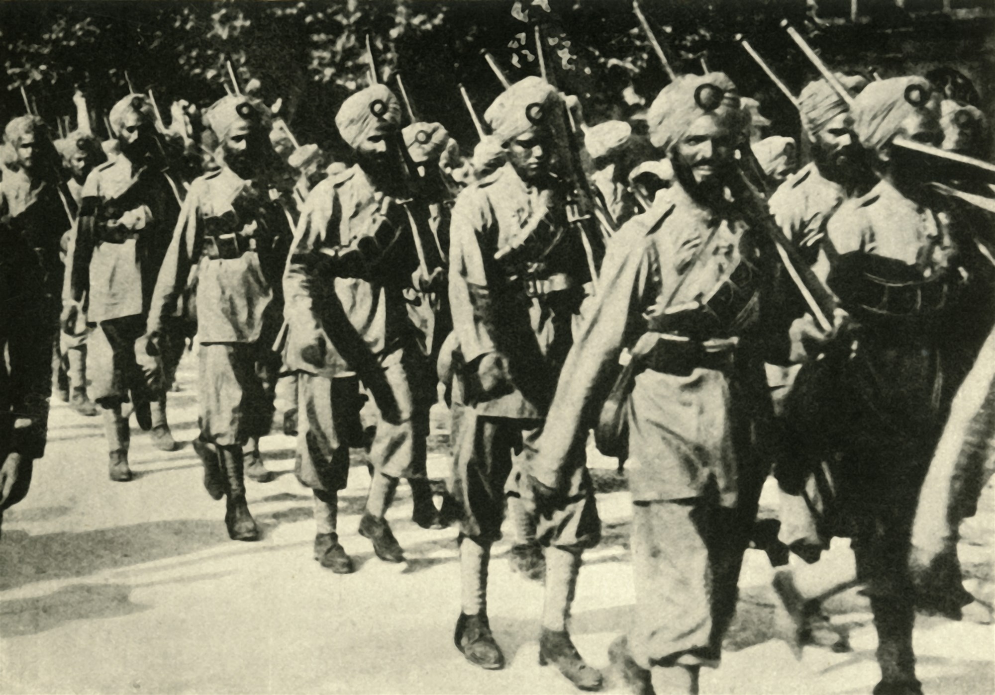 Black and white photo of Indian soldiers marching in uniforms with guns.